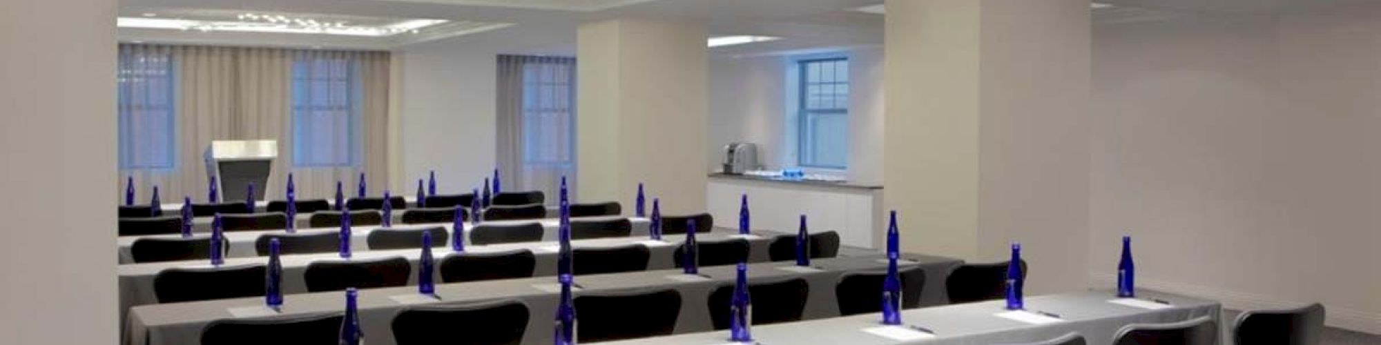 A modern conference room setup with rows of tables and chairs, each spot equipped with a notebook and a blue water bottle, well-lit and ready.