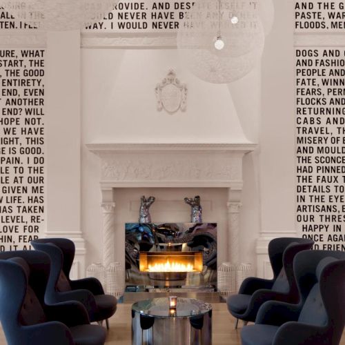 This image shows a modern living room with a fireplace, black armchairs, and text-covered walls featuring various phrases and sentences.