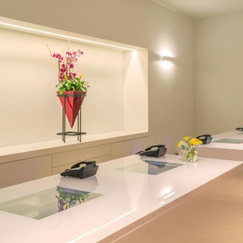 The image shows a minimalist reception area with three counters, each with a telephone and flowers. A decorative vase is displayed on the wall.