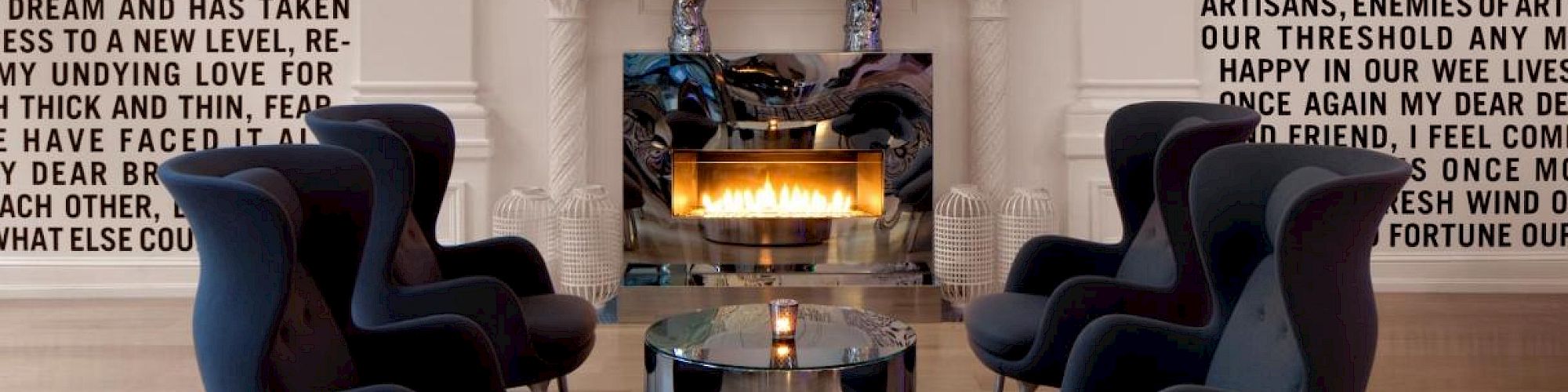 A modern living room with a fireplace, black chairs, a glass coffee table, and walls covered in large, block-text quotes or passages.