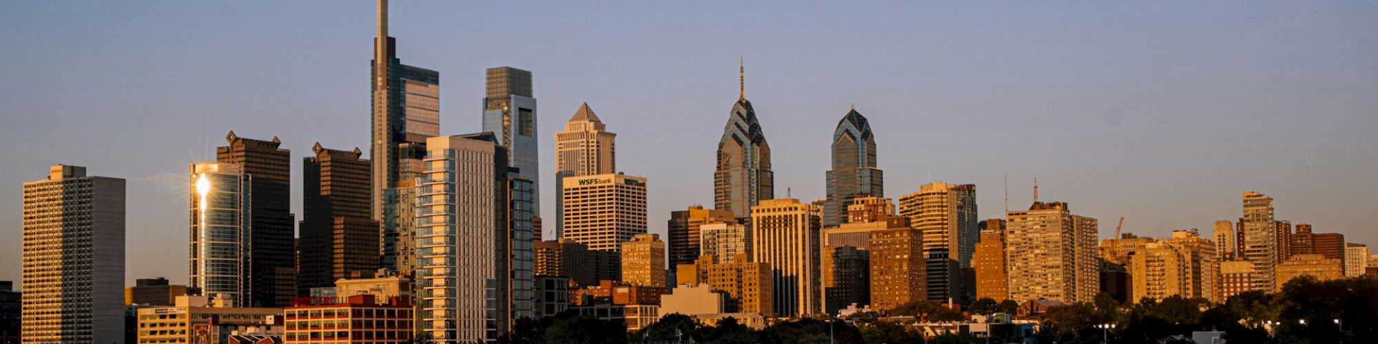 The image shows a city skyline at sunset, with tall buildings reflecting sunlight, and a river in the foreground, ending the sentence.